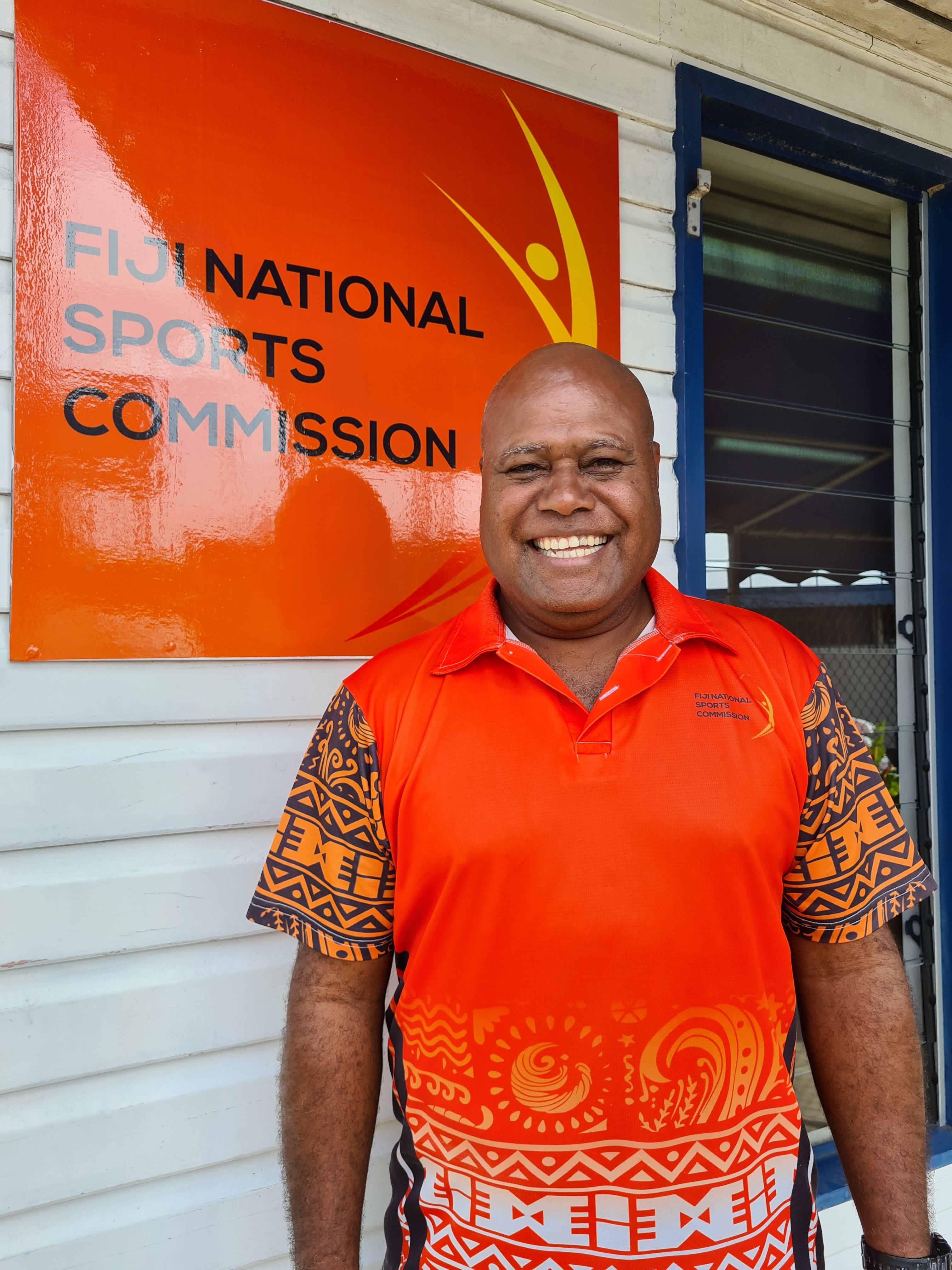 Photo of Mr Joe Tuinamata wearing a bright orange t-shirt with the Fiji National Sports Commission logo